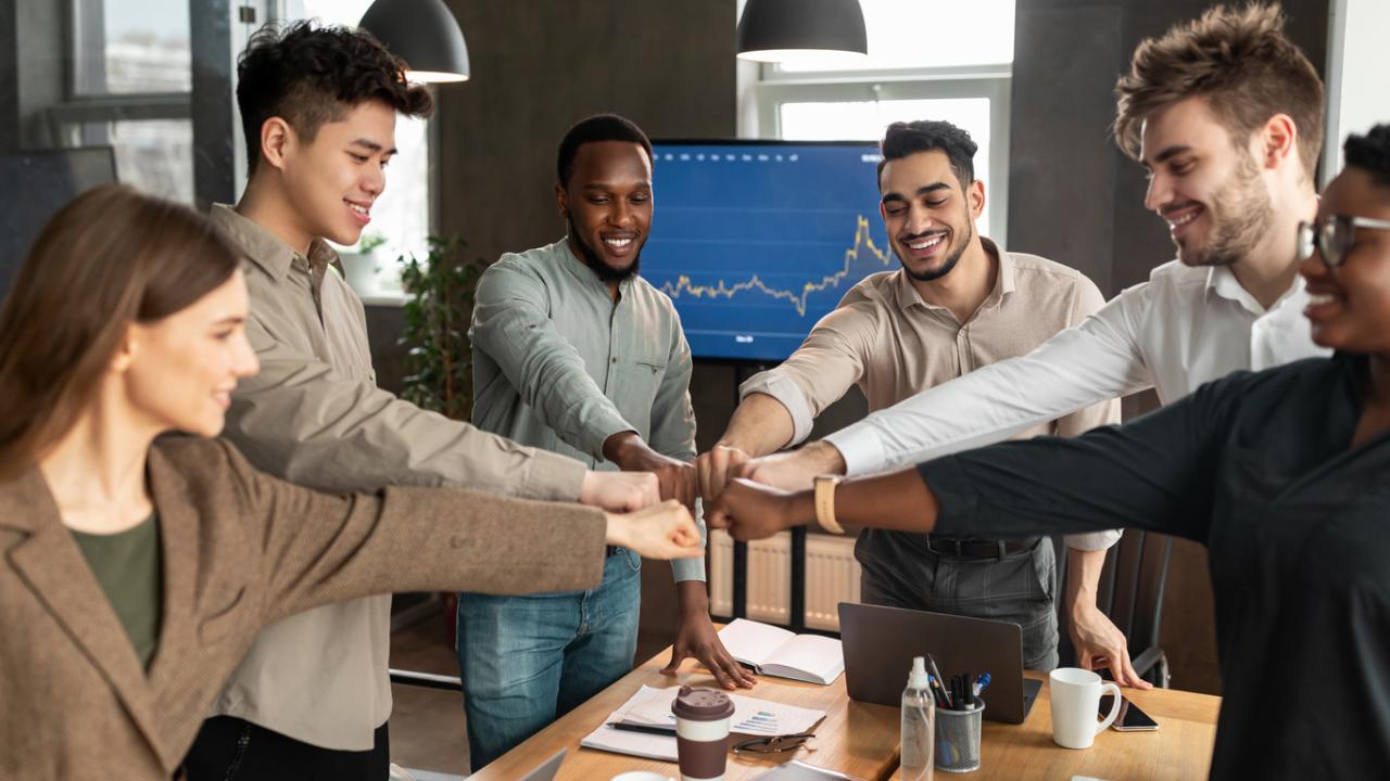 Image of a diverse team of works joining together in a fist bump.