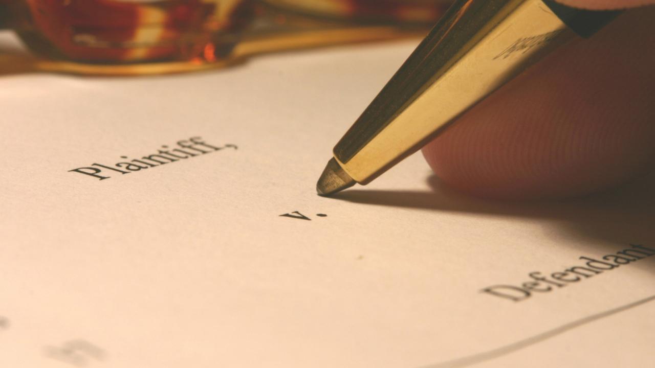 Image of a pen poised over a document that reads, in part, "Plaintiff v. Defendant."