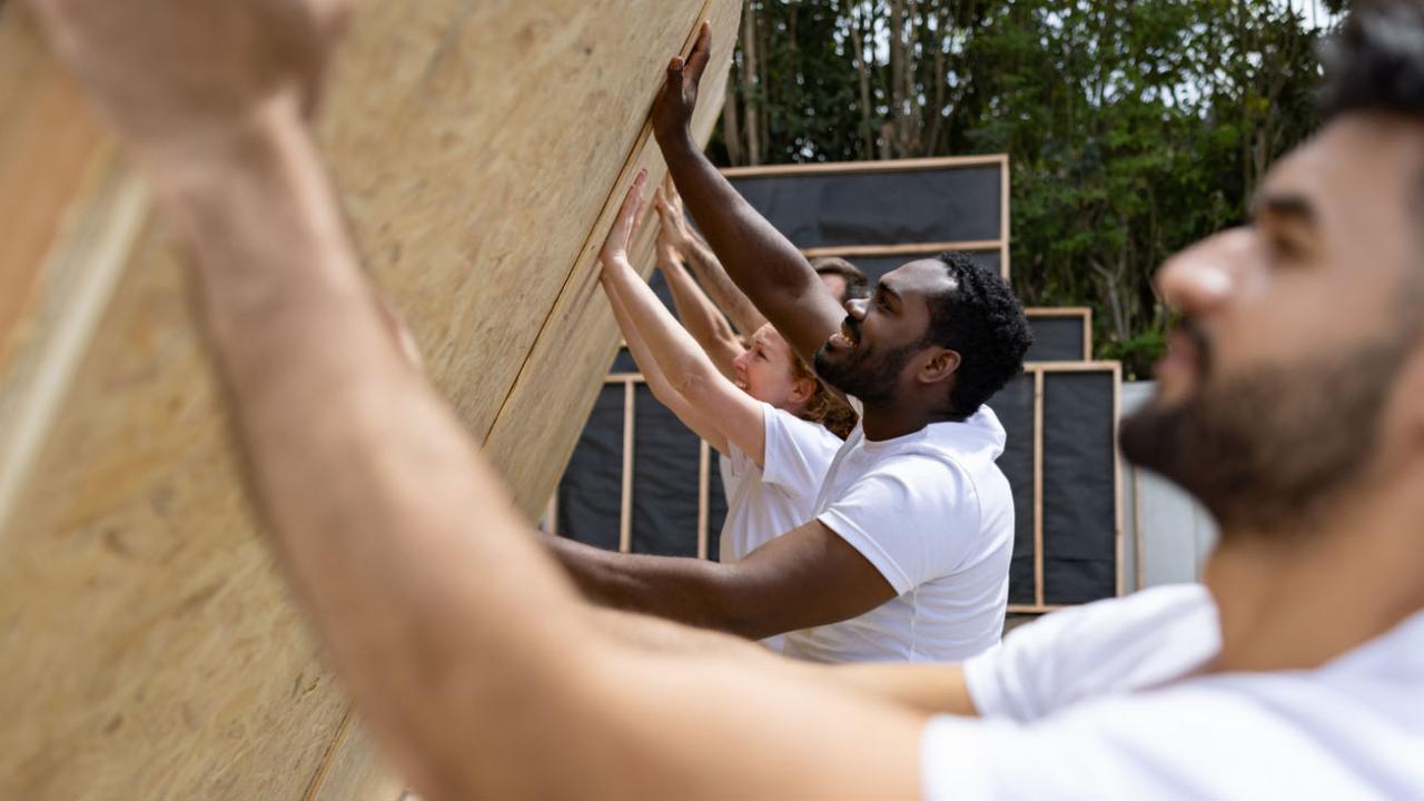 Image of a group of volunteers raising a wall for a new home under construction.