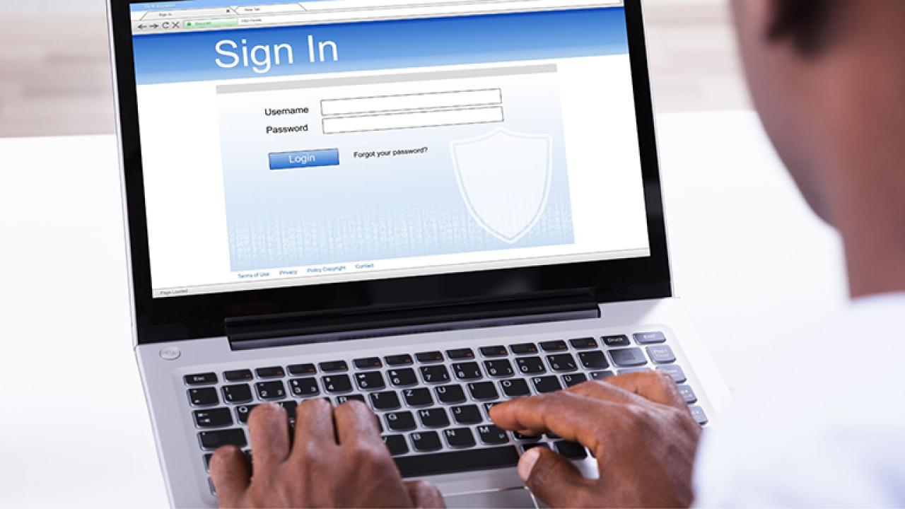 A person is typing on a laptop with a login page visible on the screen.