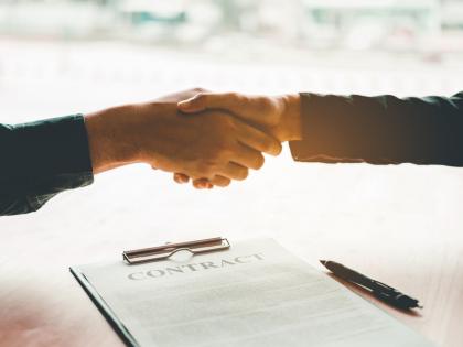 A pair of hands shake over a document labeled "contract."