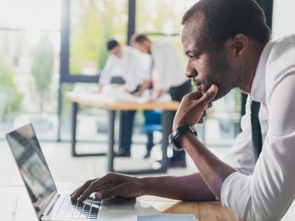 Image of a man starting at a computer screen, deep in thought, with his chin on his hand.