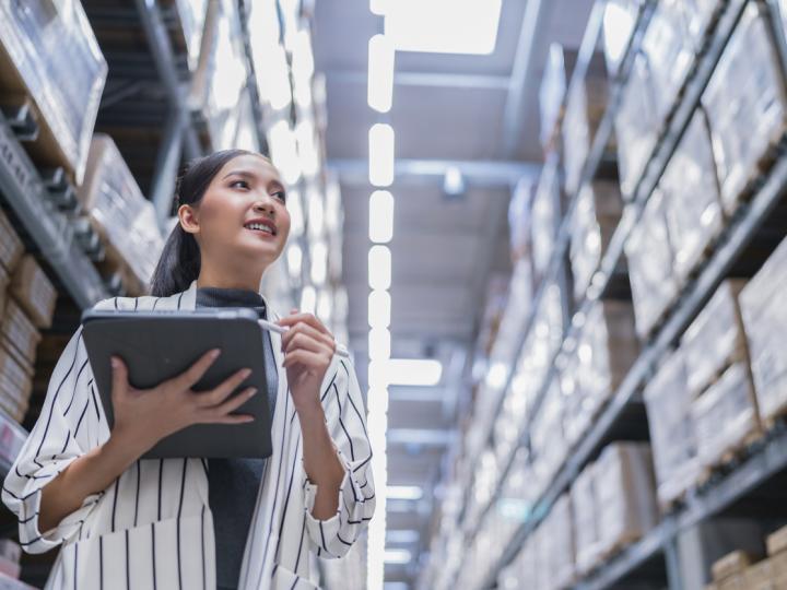 A smiling woman with a tablet reviews inventory in a warehouse.