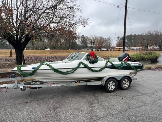 Image of a speed boat sitting on trailer. The trailer holding the boat sits in a parking lot. The boat is decorated with Christmas garland and a Christmas wreath. 