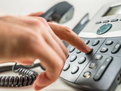 A hand pushes buttons on a desktop telephone.
